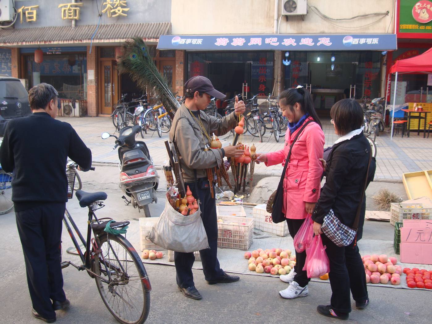 Picture:  An ambulatory music store.  The young man is selling flutes and Chinese violins and hú lu sī (gourd reed flutes) on the streets of Shitang Cun, Wuxi, China