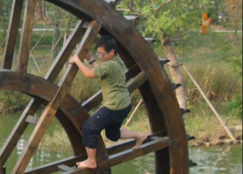 picture: A child plays on the waterwheel, which seems to have no other purpose.  Canal side park near Jiangnan University, Wuxi, China